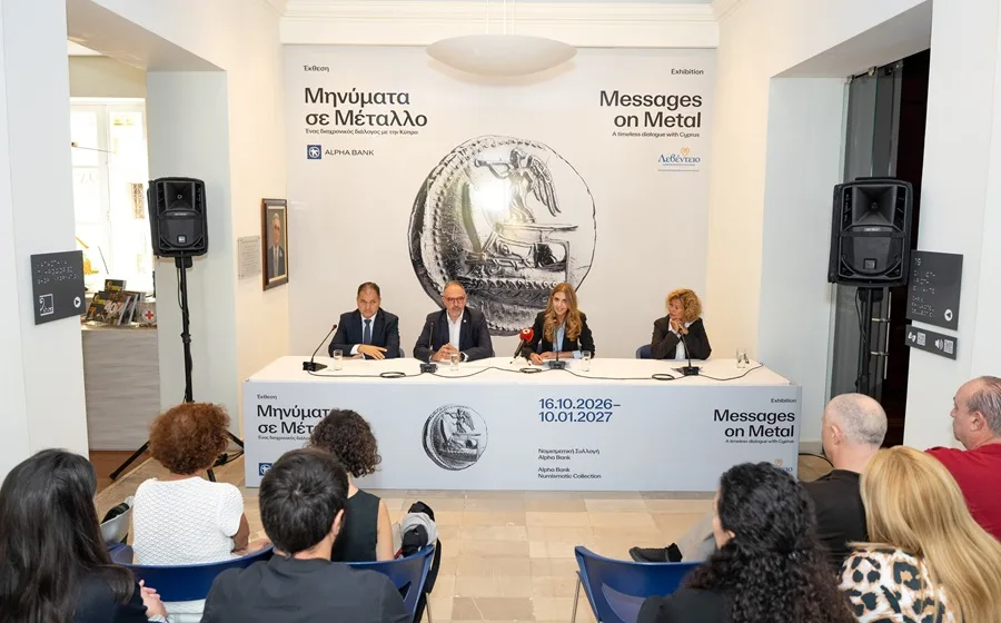 Four speakers seated at a white table in a museum hall, presenting to a seated audience, under a banner showing a large silver coin and the title Messages on Metal in Greek and English