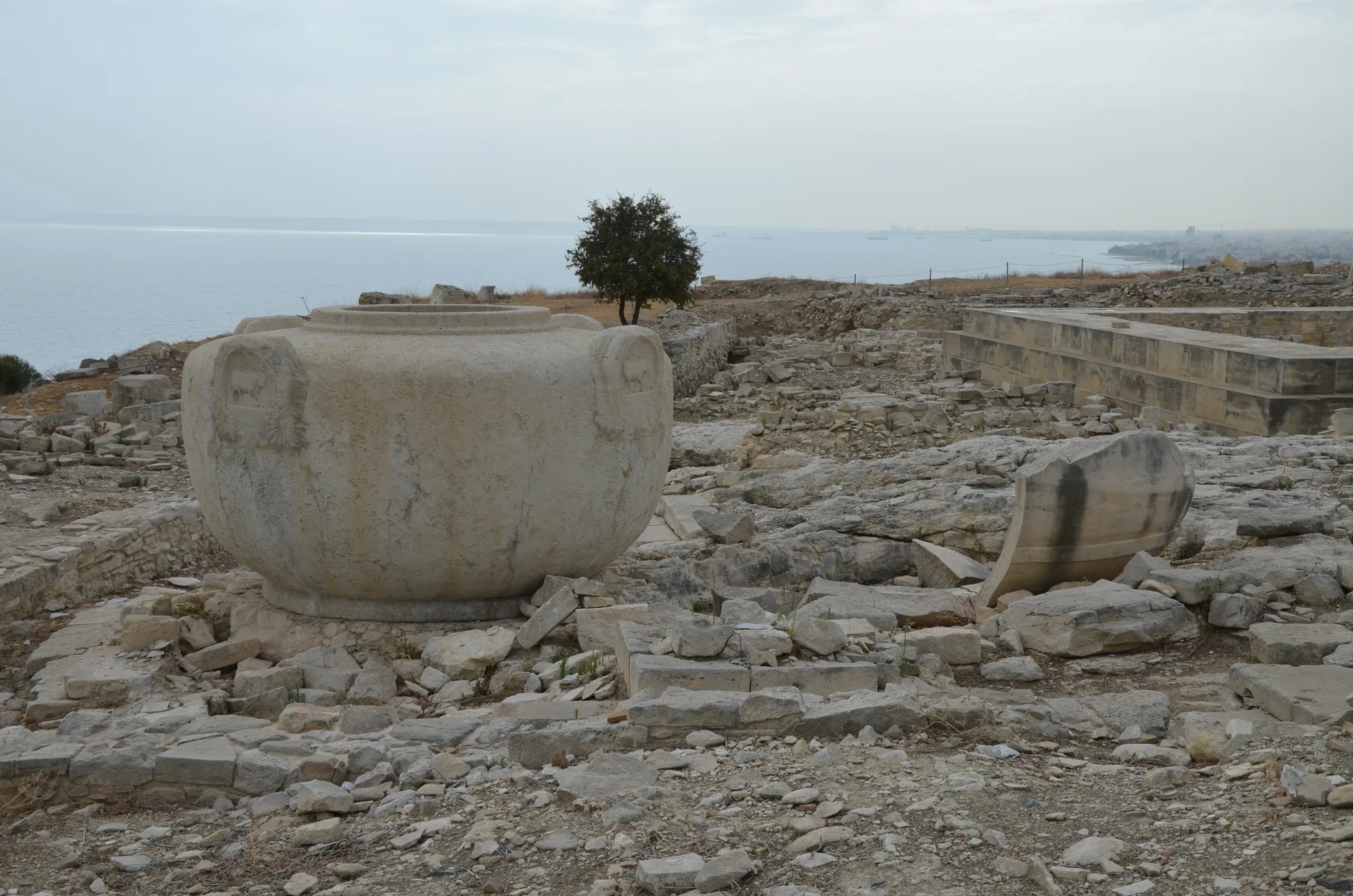 A very large stone jar with four lug handles on a rubble terrace above the sea
