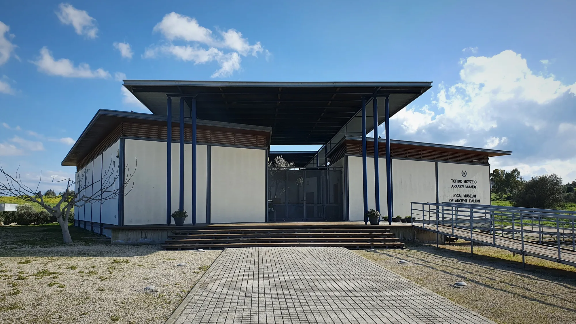 The flat-roofed white and blue entrance front of a small museum building under a blue sky