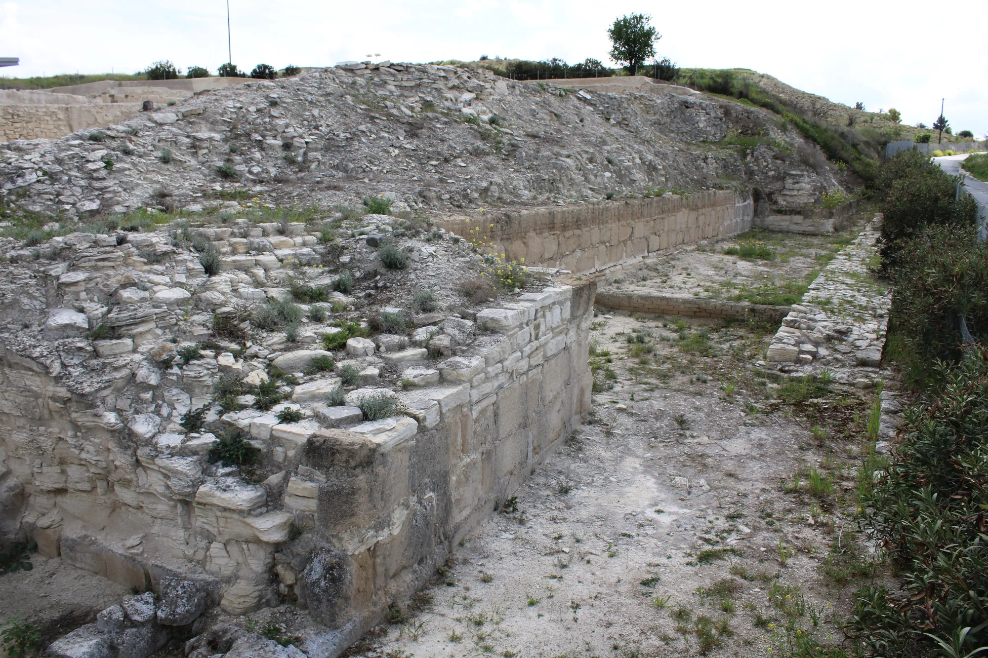 A massive stone wall and sloping rampart beside a gravel path, with trees behind