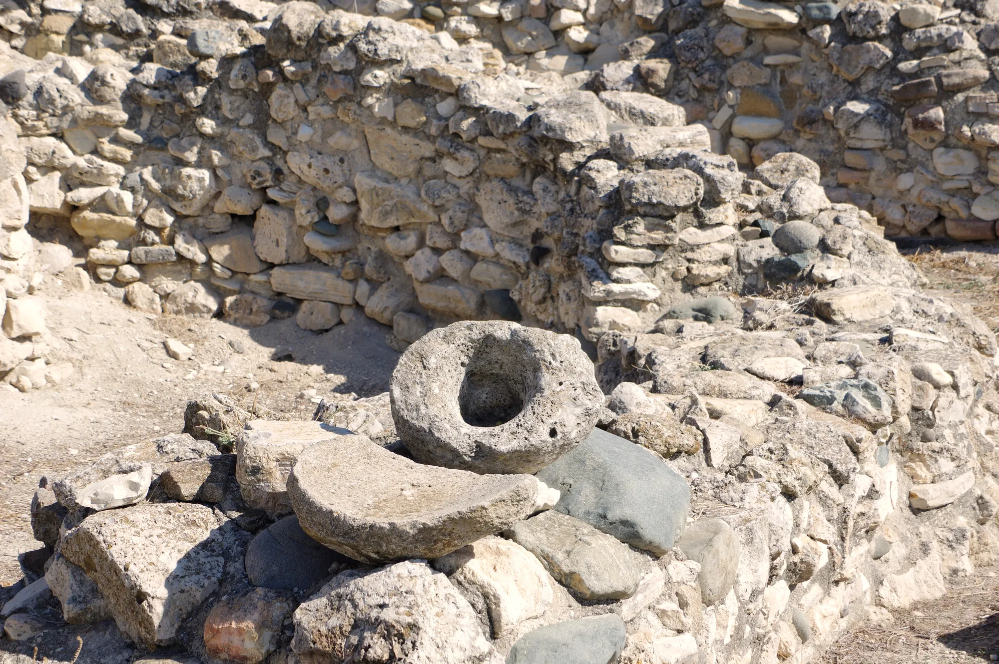 Stone mortar and grinding slab beside an excavated house wall at Khirokitia. Photo: Berthold Werner, CC BY-SA 4.0, via Wikimedia Commons
