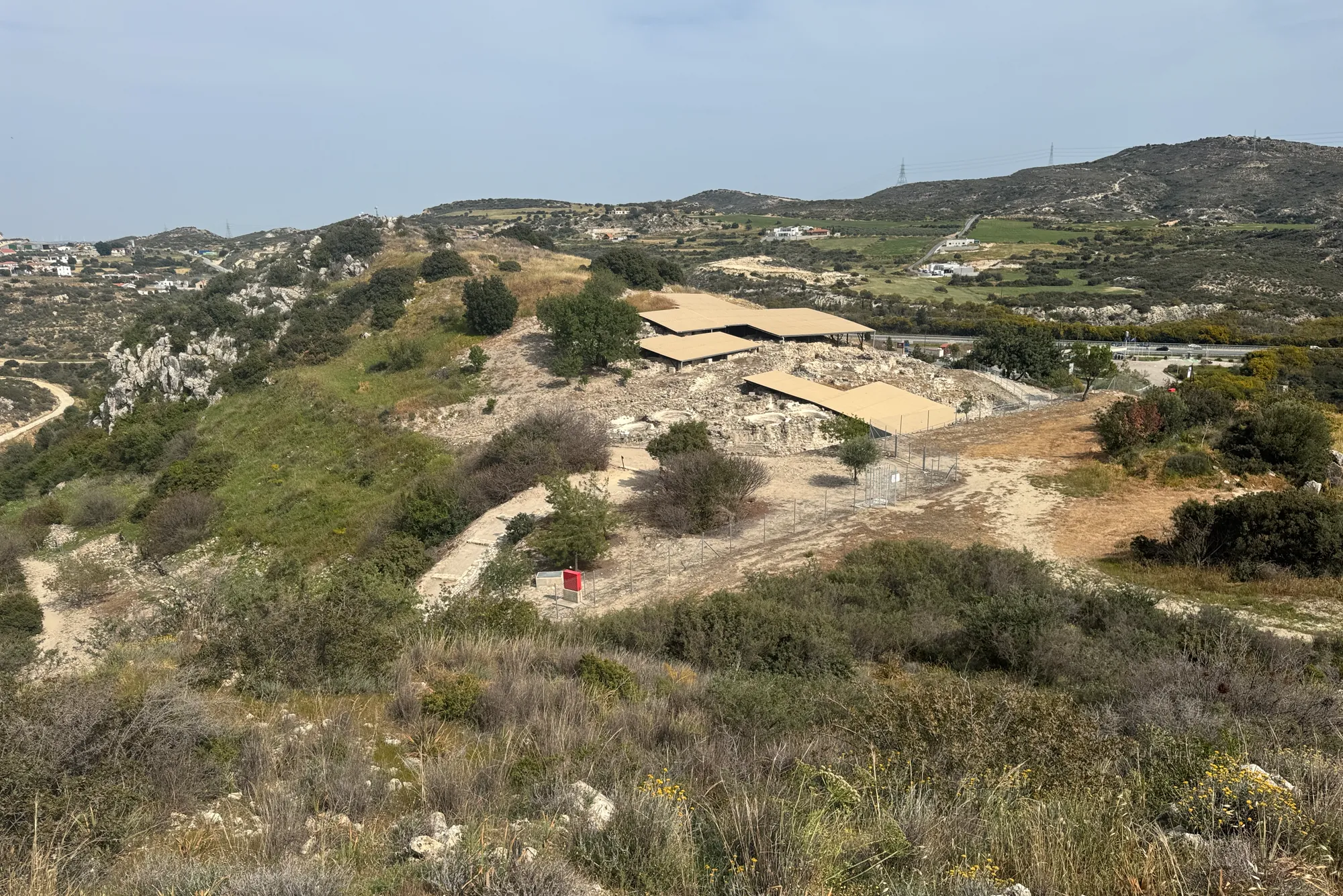 The Khirokitia excavation in its river valley, seen from the slope above, with modern roofed shelters over parts of the site. Photo: RSchreg, CC BY-SA 4.0, via Wikimedia Commons, cropped