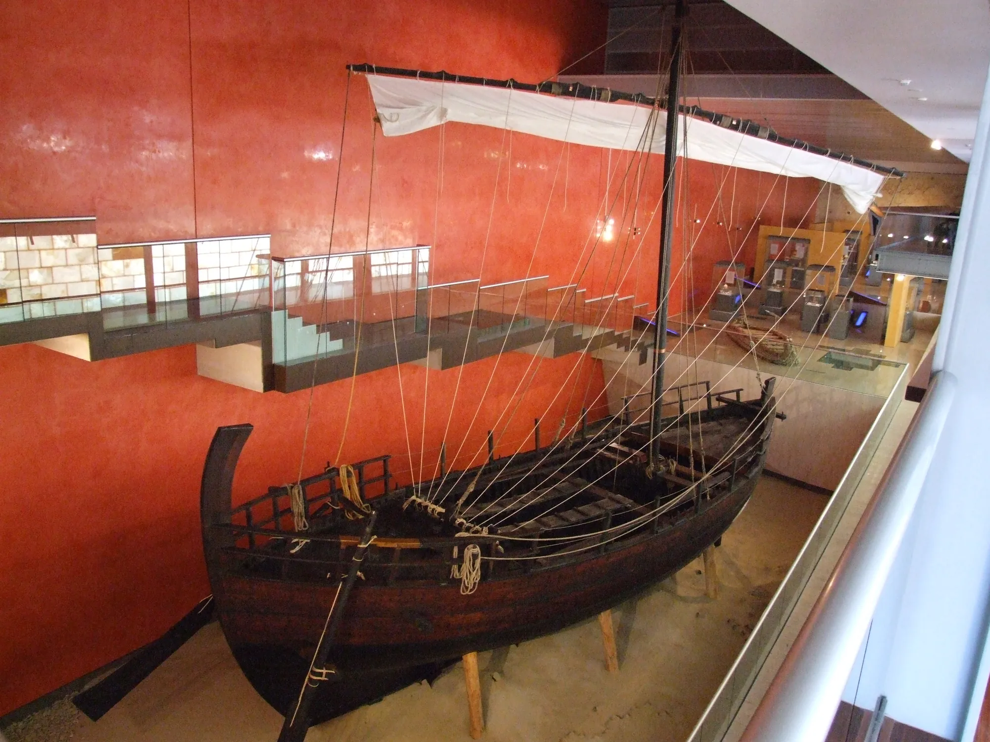 A full-size wooden replica of an ancient sailing ship with mast and rigging, displayed in a museum hall