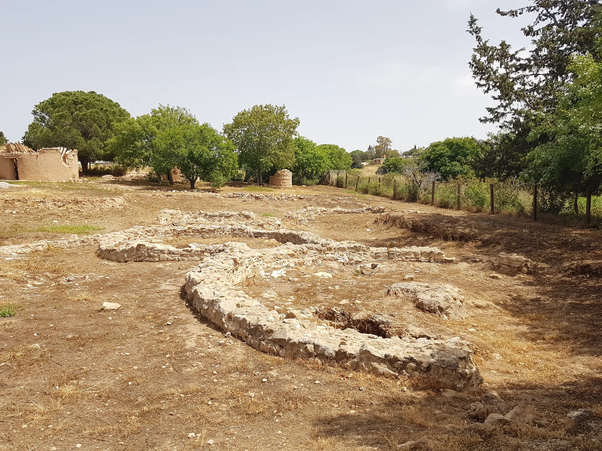 Curved stone footing of an excavated house at Lemba-Lakkous, with modern reconstructed round houses behind. Photo: Joostik, CC0, via Wikimedia Commons