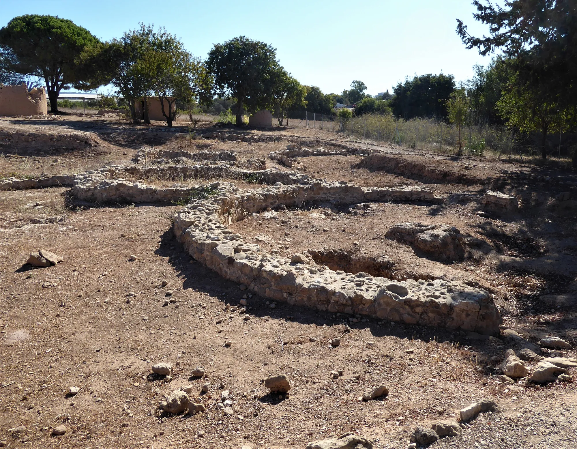 Footings of adjoining round buildings at Lemba-Lakkous, with the reconstructed houses of the experimental village beyond. Photo: Chris06, CC BY-SA 4.0, via Wikimedia Commons