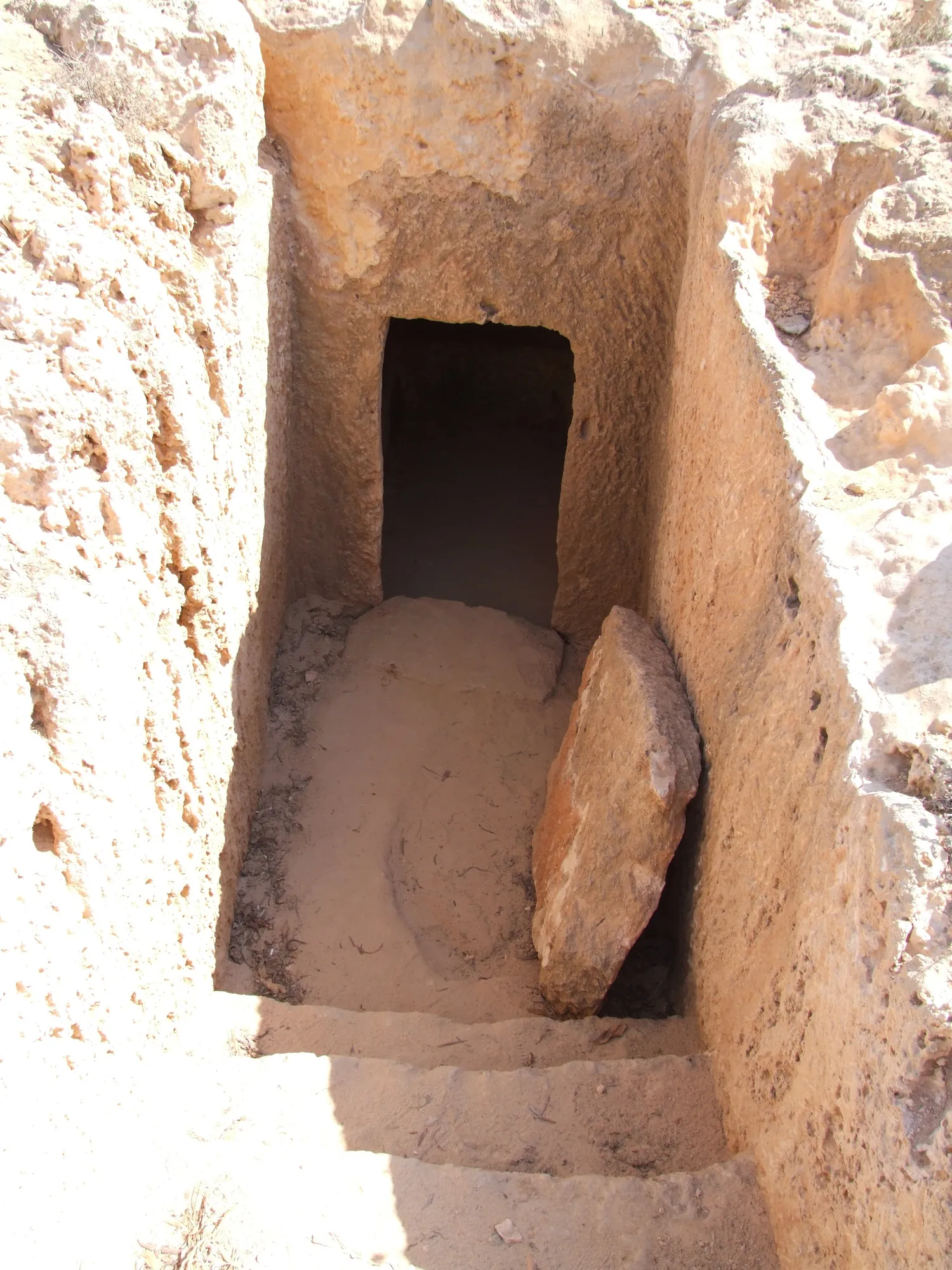 A rock-cut stairway leading to a doorway, with a large flat stone slab propped against one side