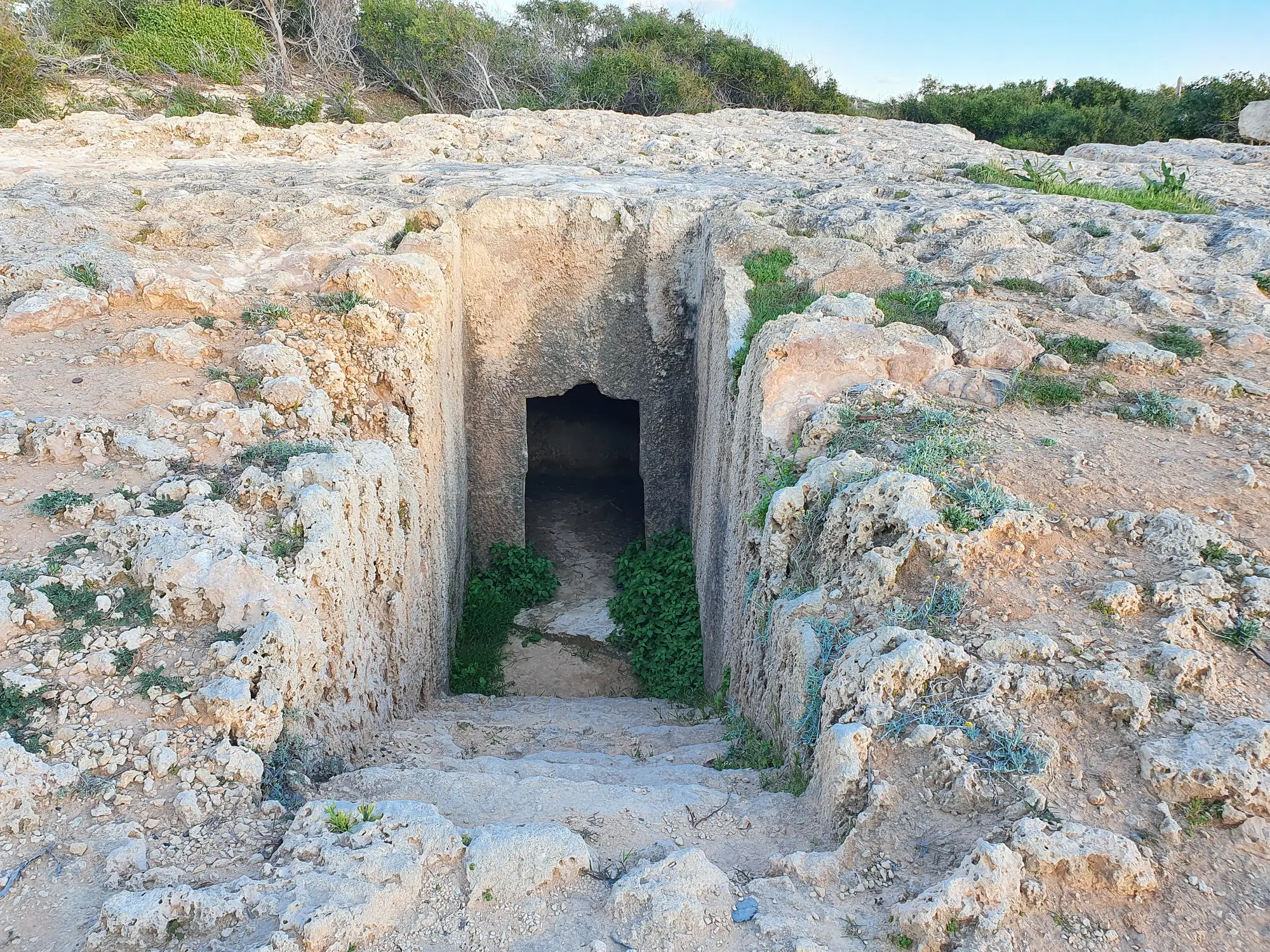 A stepped dromos cut into the rock of the promontory leads down to the doorway of one of the tombs. Photo: Qasinka, CC0, via Wikimedia Commons.