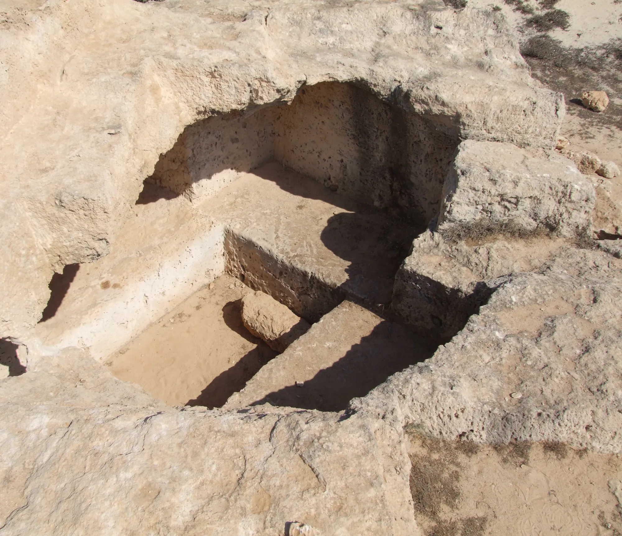 An open rock-cut pit seen from above, with a rectangular trench between two raised ledges