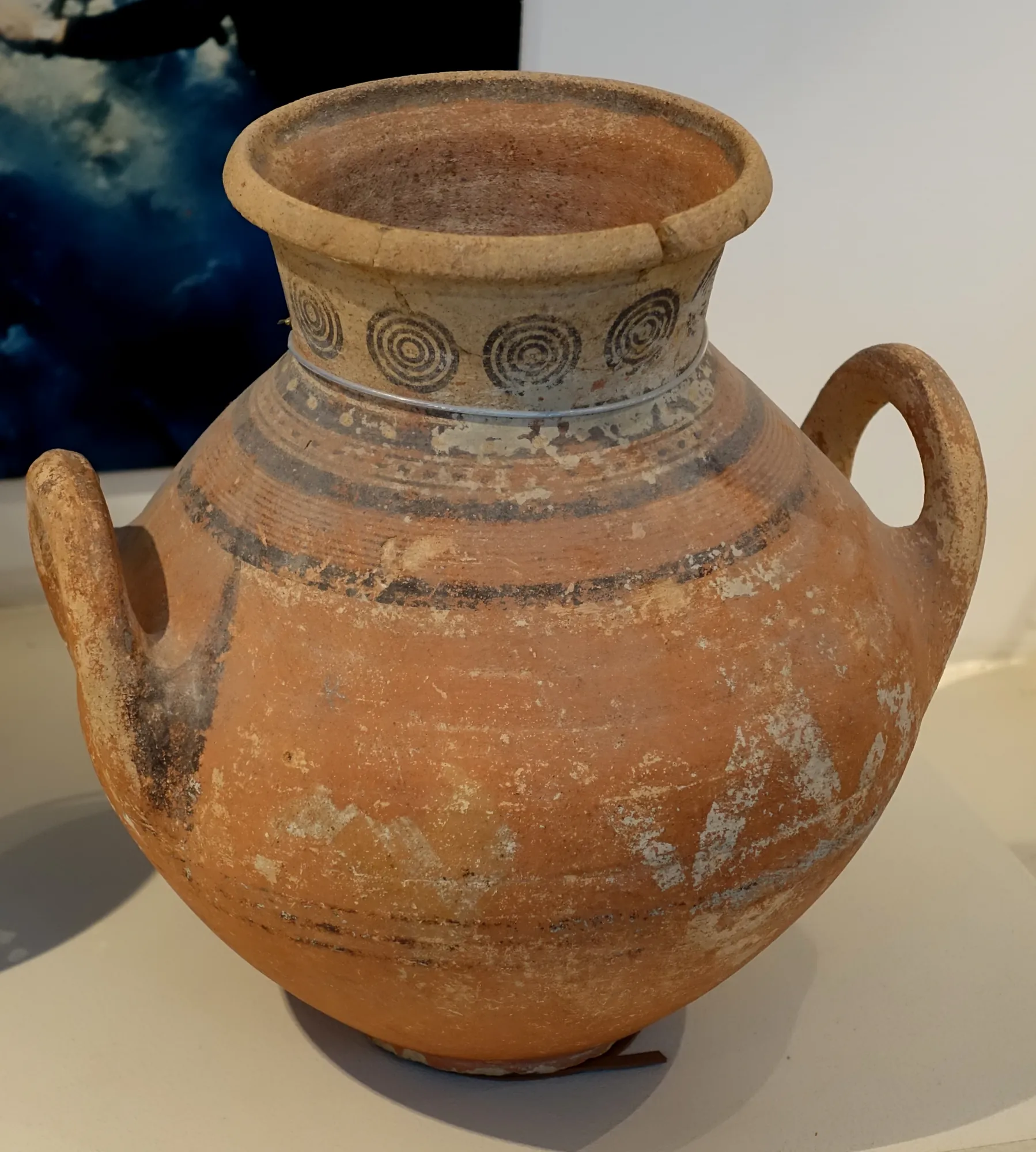 A two-handled red pottery krater with concentric circles painted on the neck and dark bands around the body