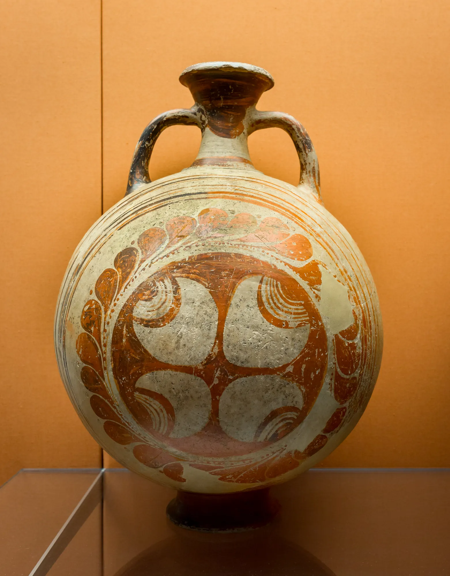 A large round-bodied pottery flask with two small handles, painted with a red-brown wheel and leaf pattern on a cream ground