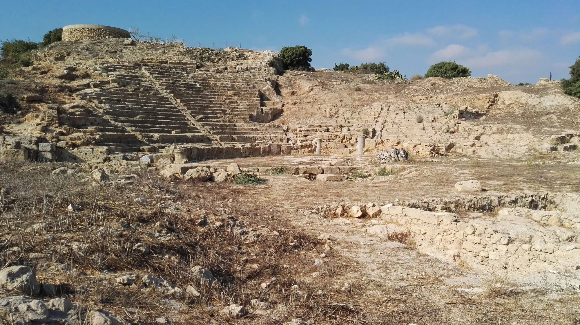 Tiers of stone seating cut into a rocky hillside above an excavated area of rubble and low walls