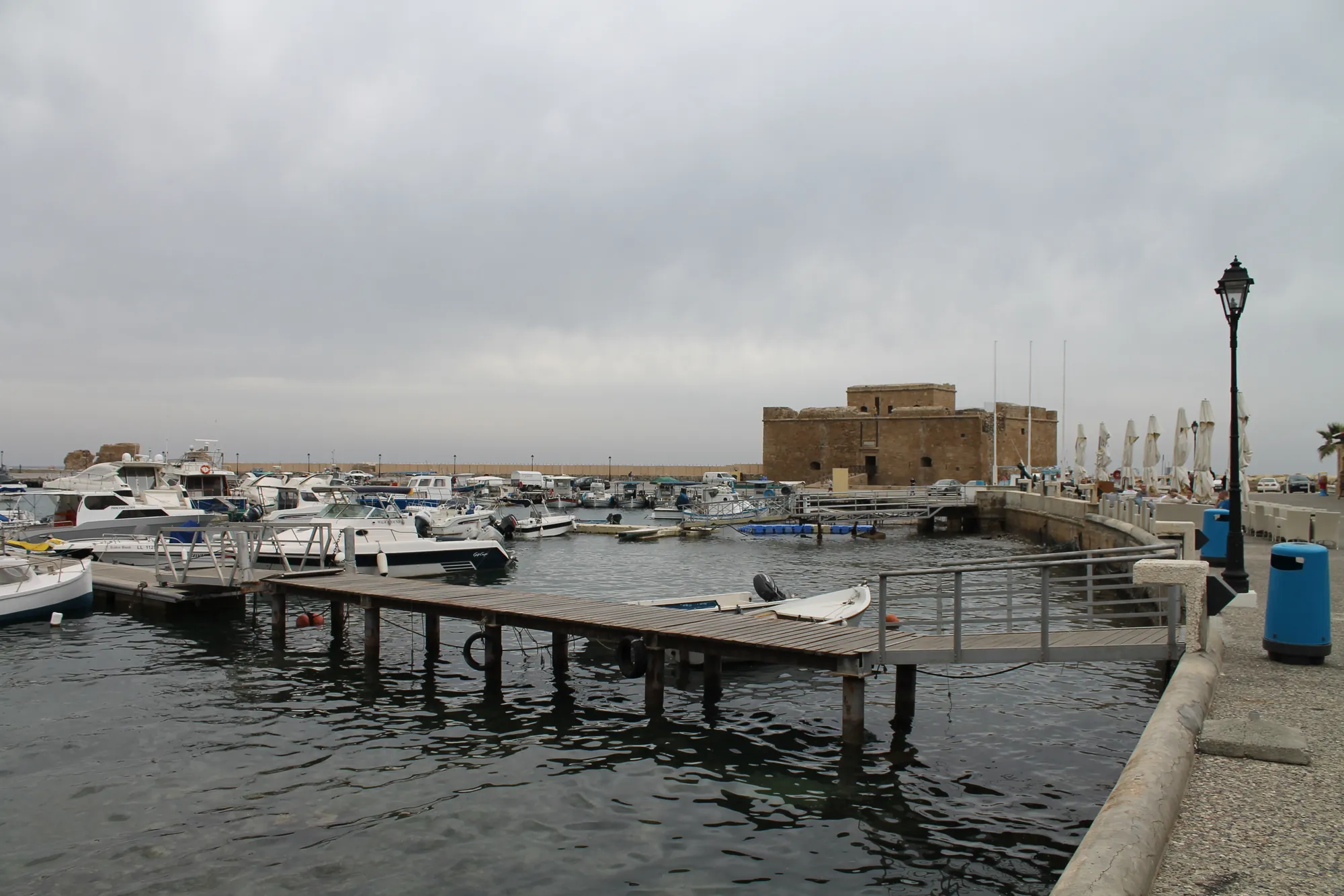 Small boats moored along a jetty in a harbour, with a square stone fort at the far end of the quay