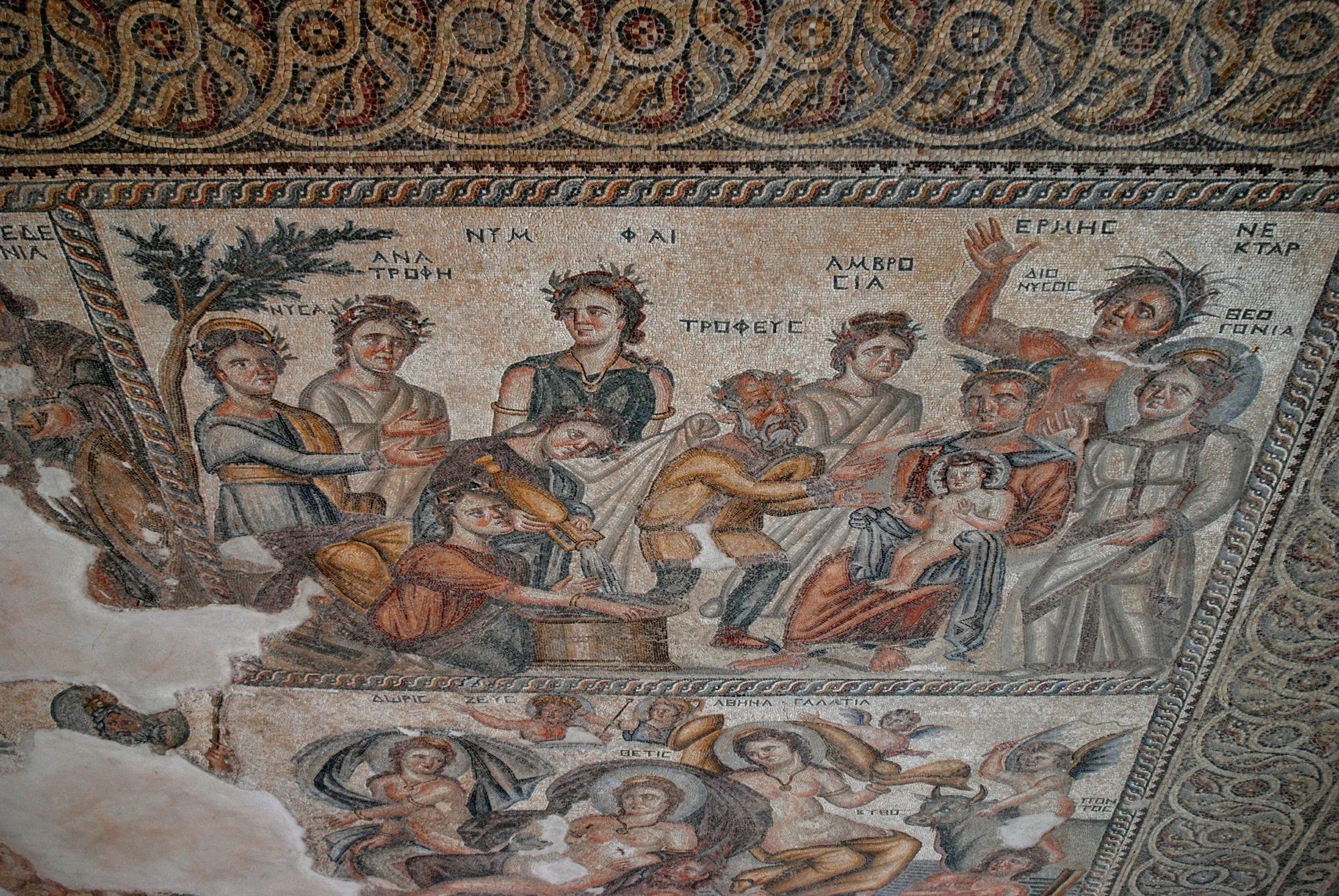 A crowded mosaic panel of robed figures with Greek name labels, a seated man holding a small child at its centre