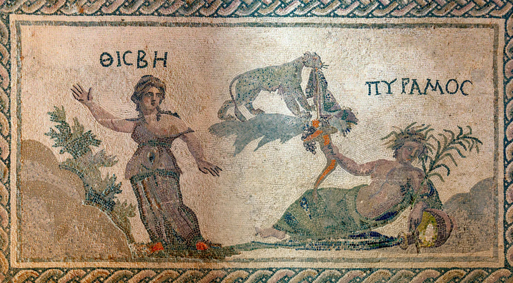 A floor mosaic of a woman with raised arms, a leopard holding a cloth, and a reclining man with a water jar, labelled in Greek