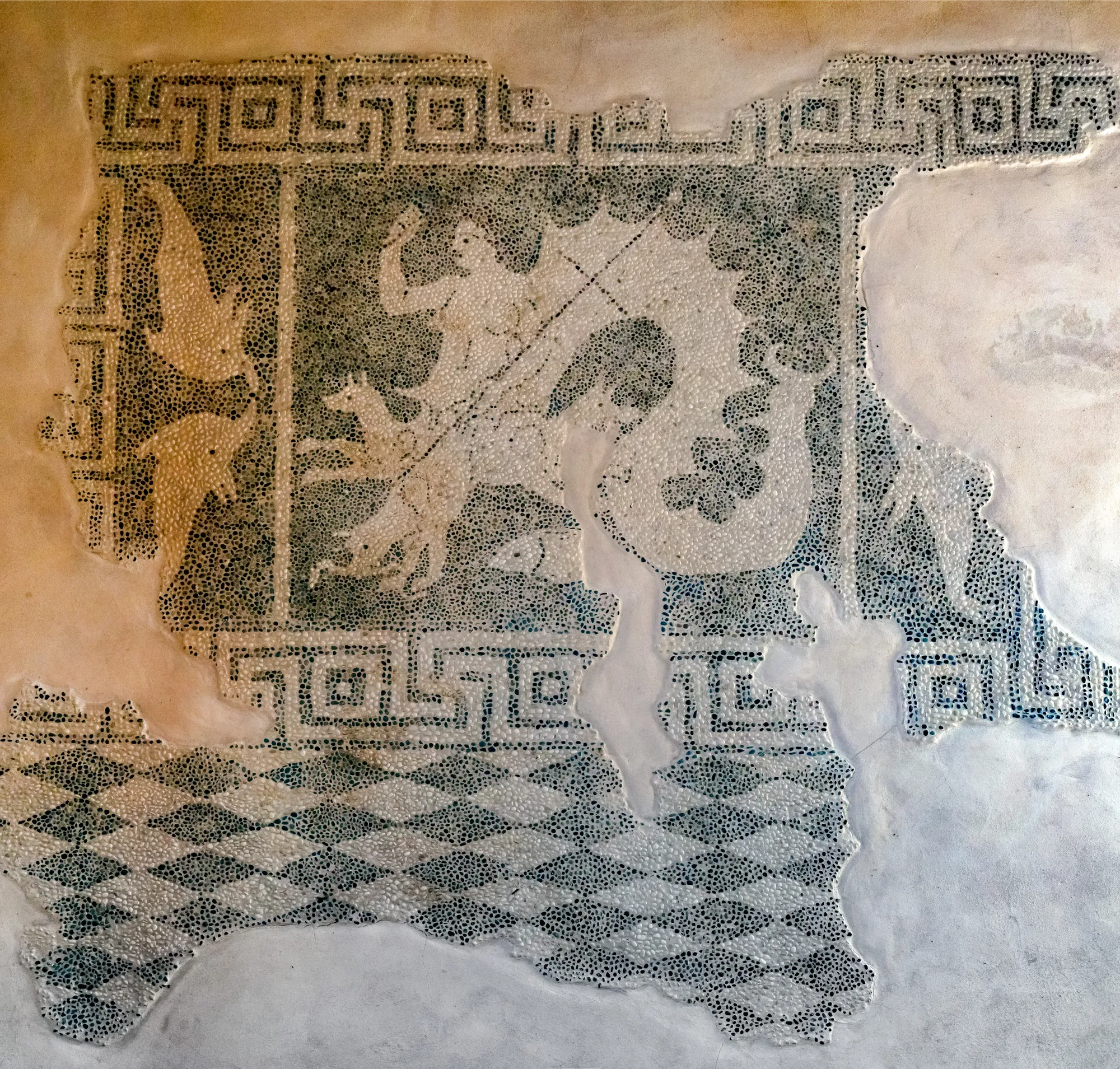A fragment of a pebble mosaic in dark and light stones showing a sea monster, framed by a meander border