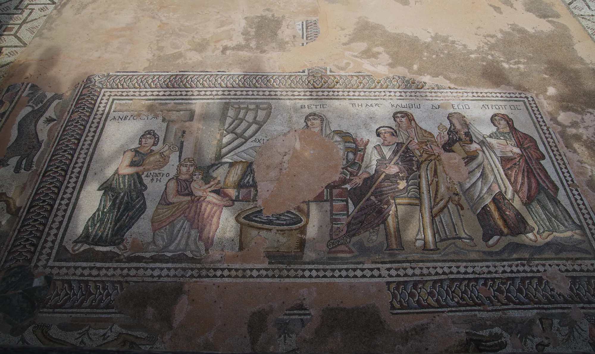 A rectangular floor mosaic of standing and seated figures gathered around a basin, inside a patterned border