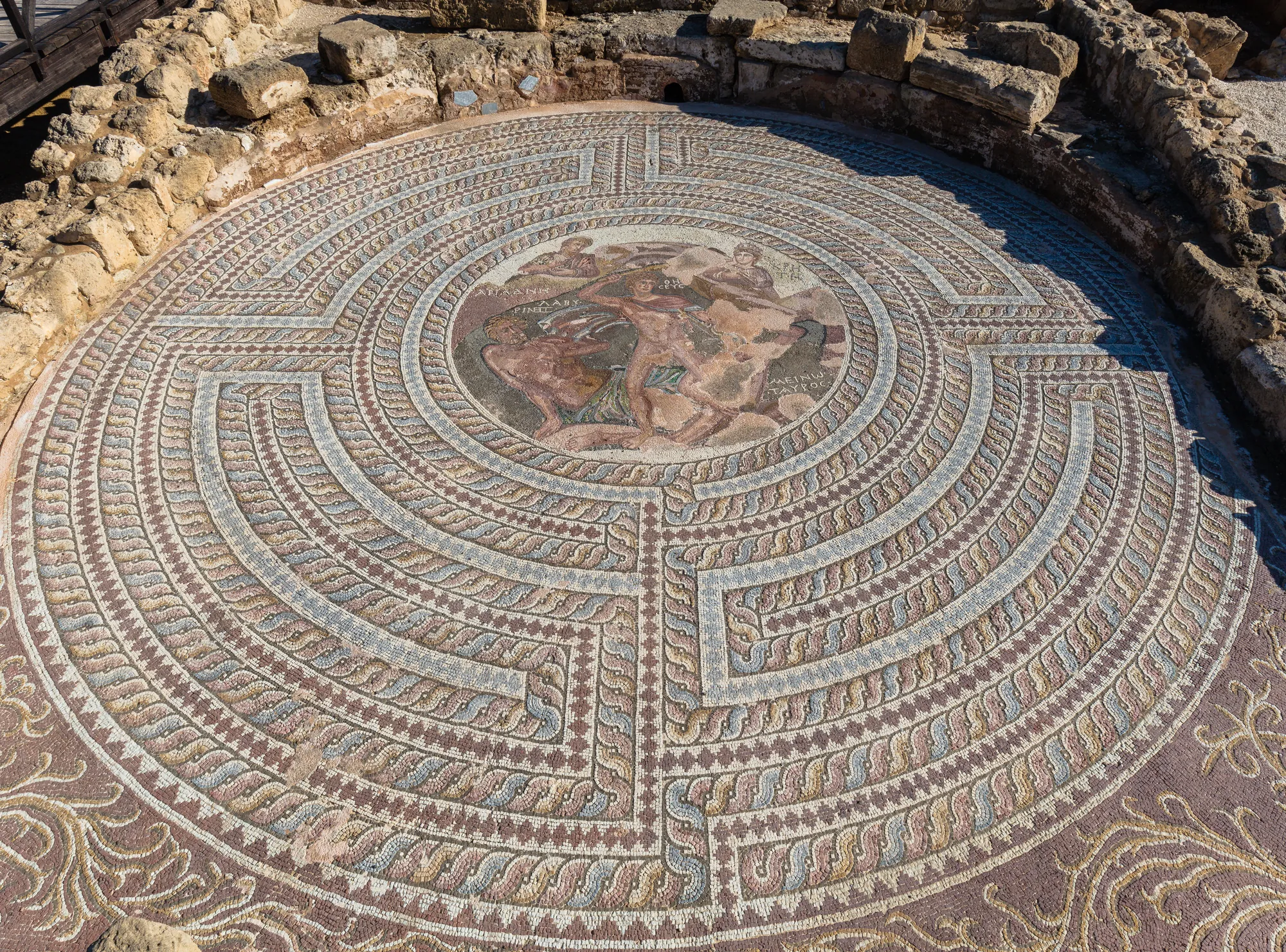 A large circular floor mosaic of concentric patterned rings around a central figured scene, seen from above