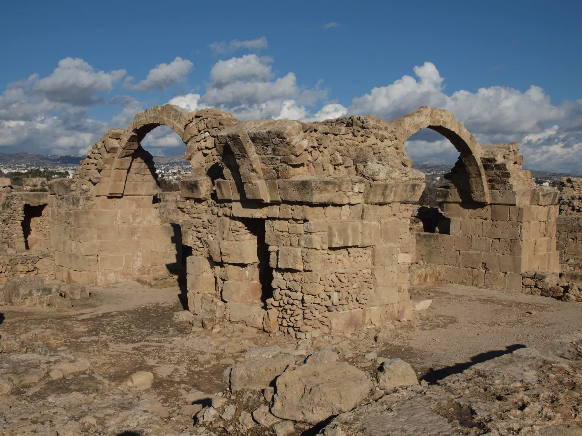 Ruined stone walls and two tall arches of a castle under a blue sky with white clouds