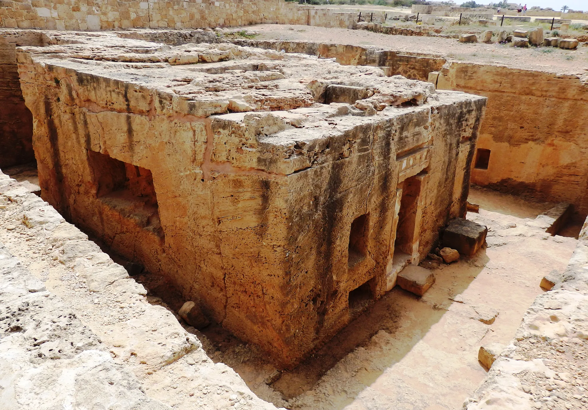 A large rectangular block of golden rock standing in a sunken court, with doorways and niches cut into its sides