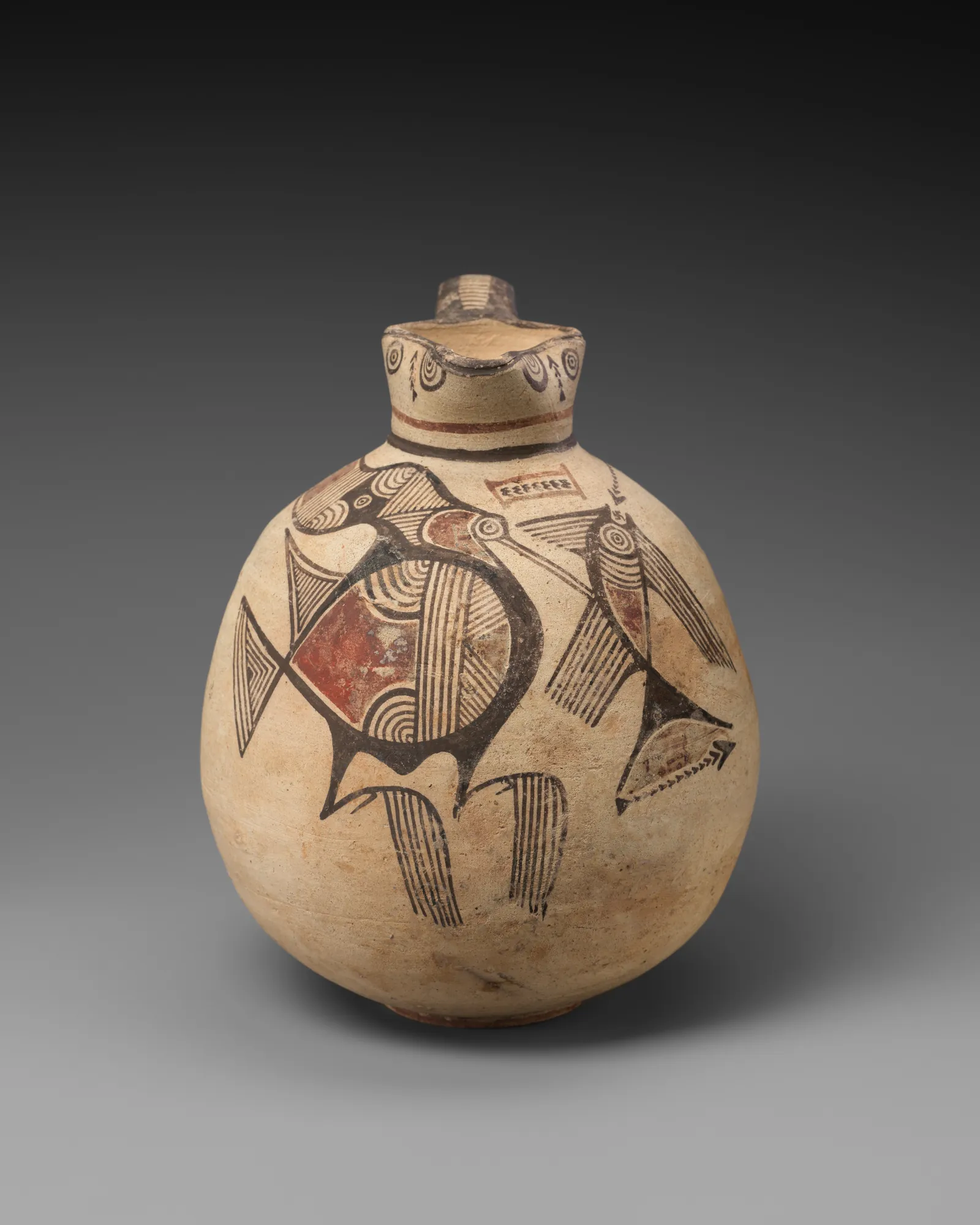 A round-bodied clay jug painted in red and black with a large bird holding a fish in its beak