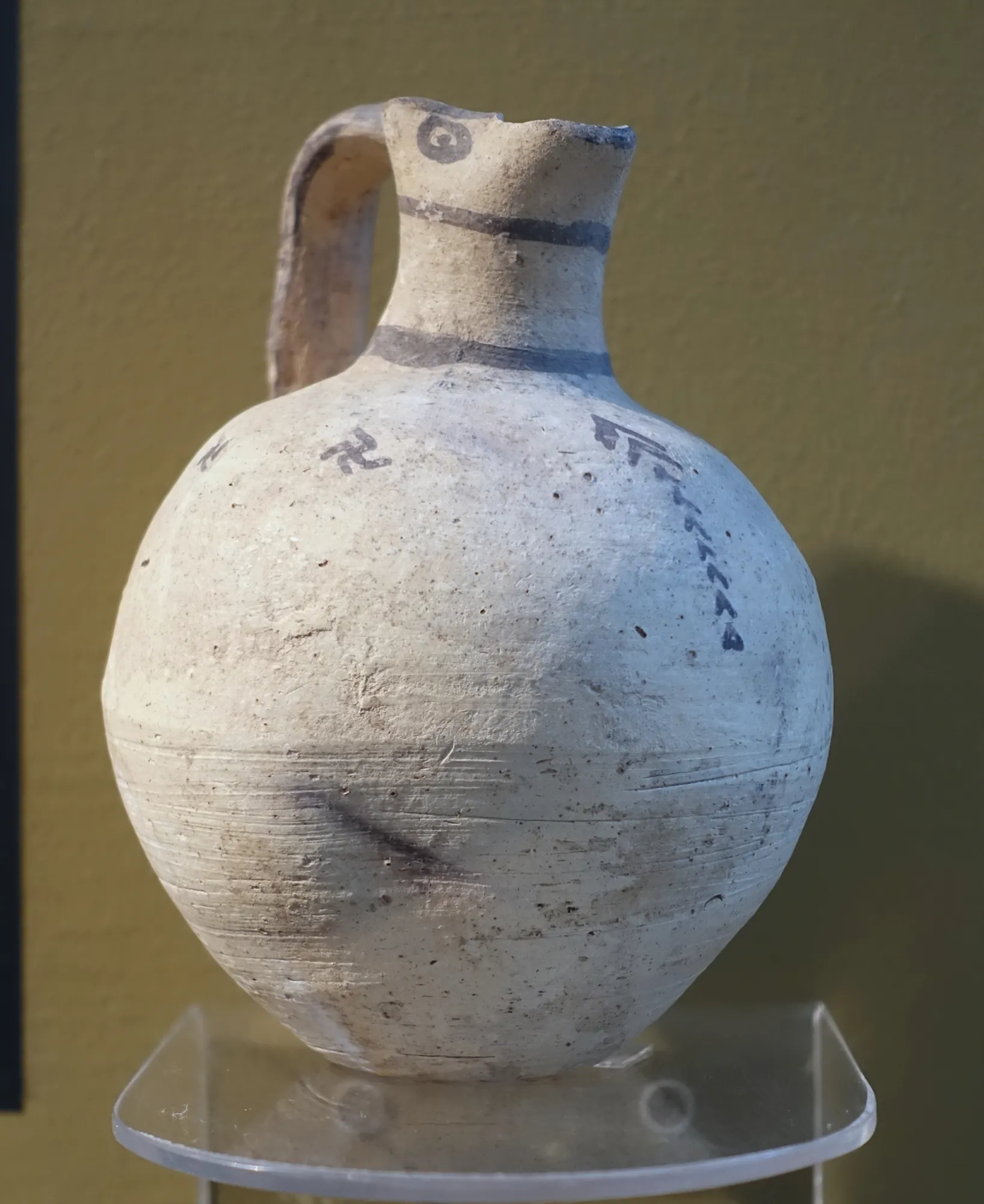 A plain round-bodied clay jug with a trefoil mouth and a few painted lines on the shoulder
