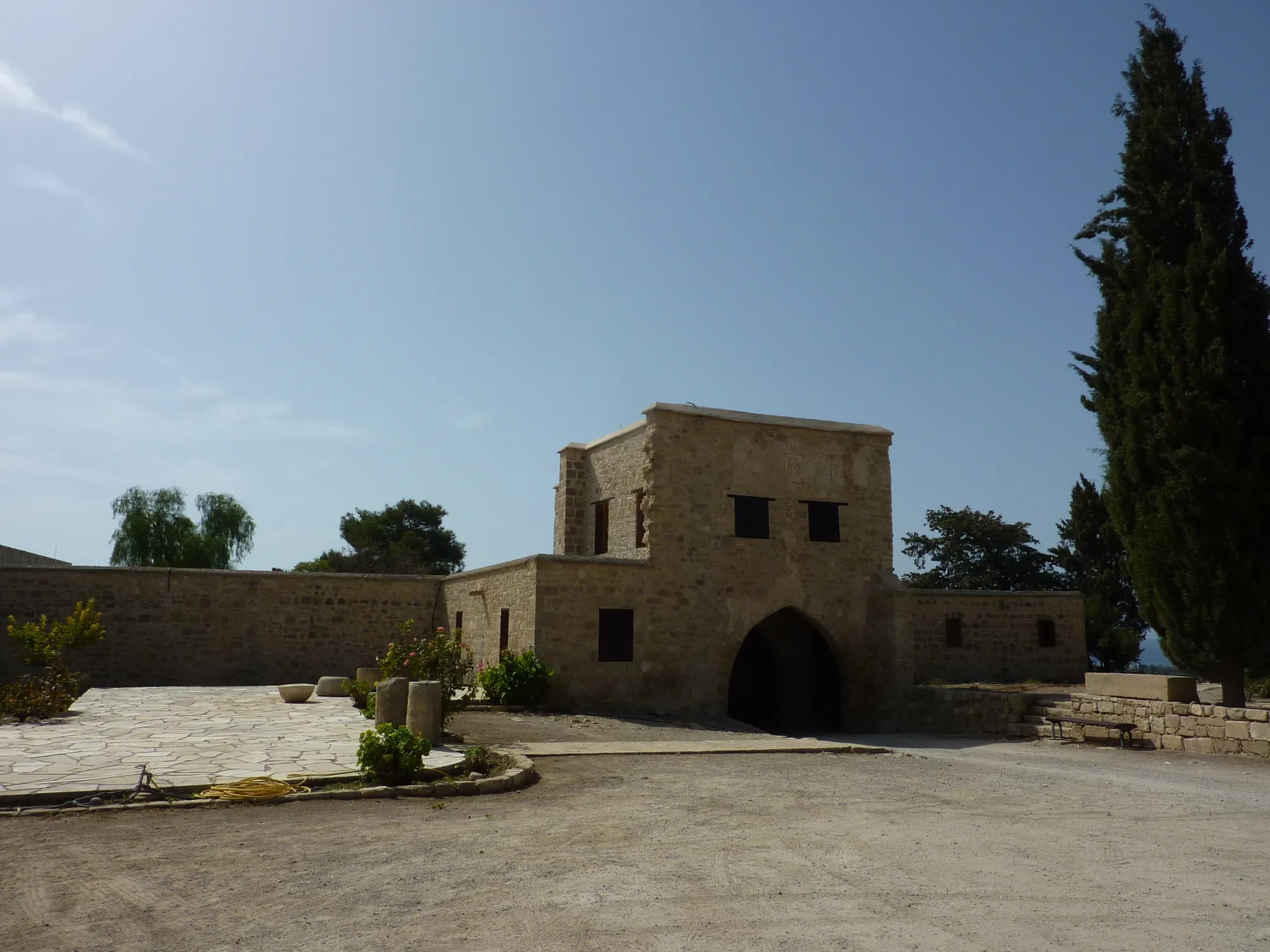 Stone courtyard with a pointed arched doorway in a two-storey stone building and a cypress at right