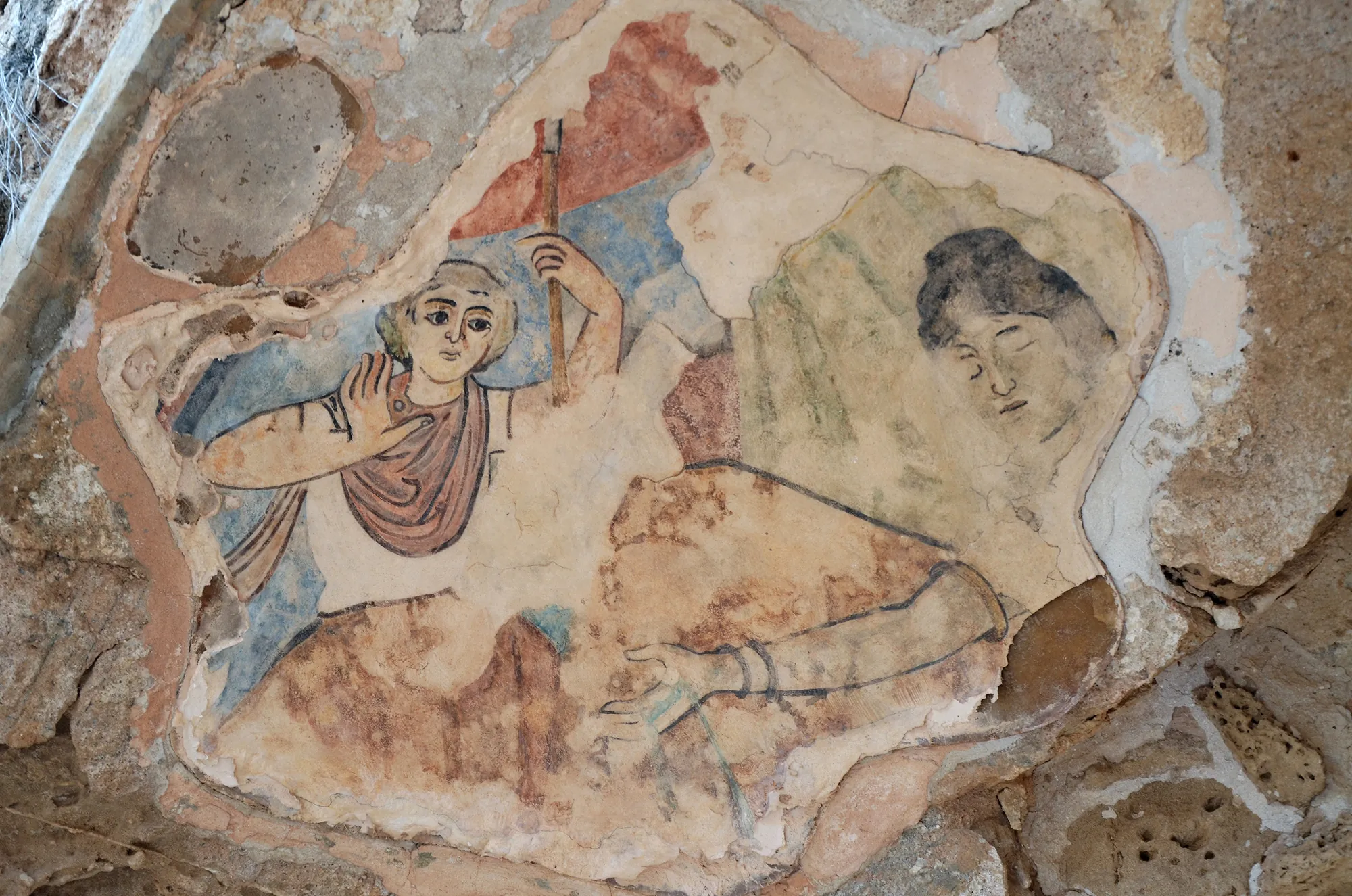 A damaged painted fresco of figures in a curved plaster niche in a ruined wall