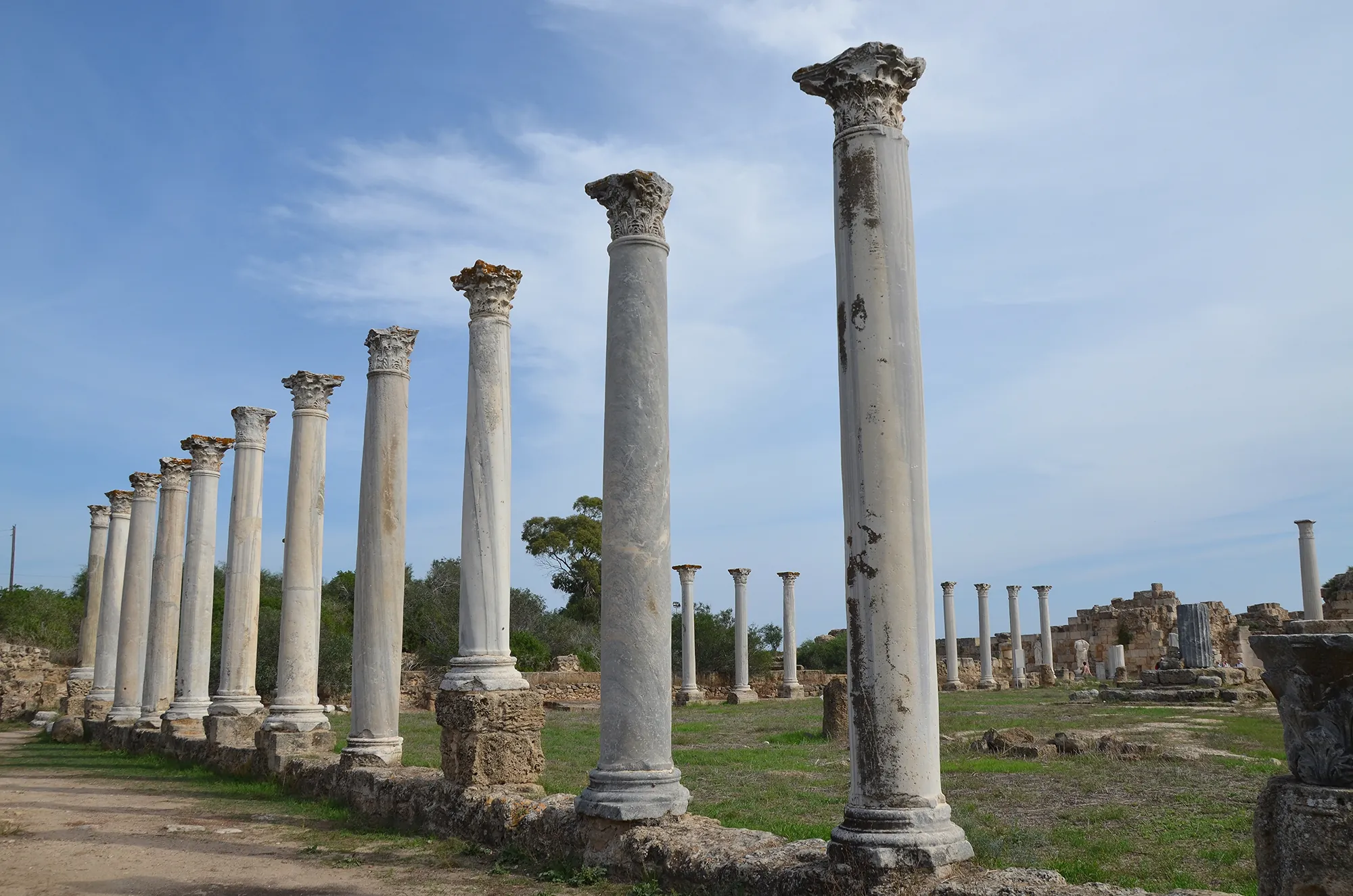 Two rows of tall marble columns with Corinthian capitals beside a paved walkway